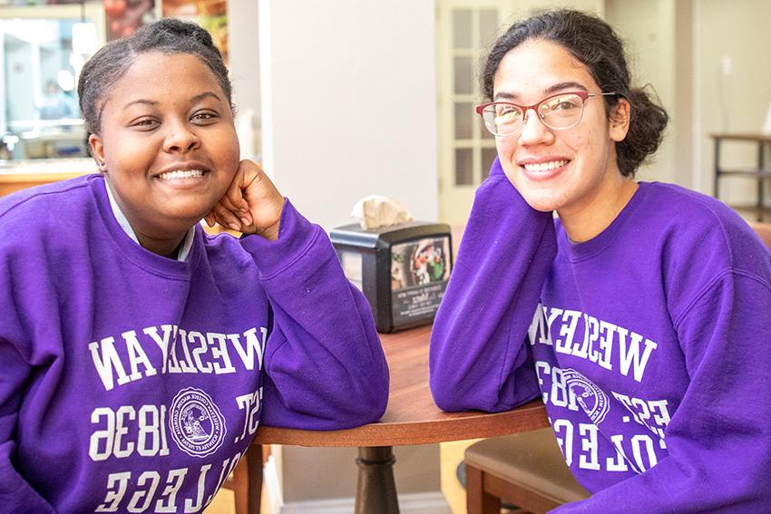 两个学生坐在桌子旁，穿着紫色的运动衫